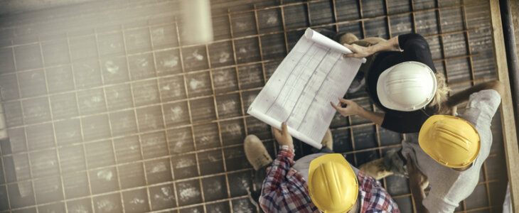 High angle view of three people with helmets, female architect, foreman and engineer on a construction site, looking down on a blueprint, copy space.