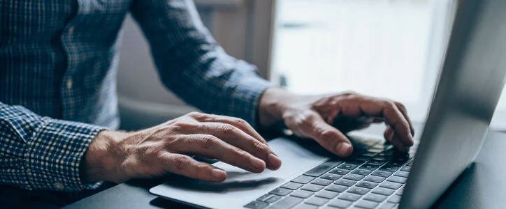 Cropped shot of a young unrecognizable businessman sitting on desk in modern office and working on laptop. Elegant handsome businessman sitting in his office and using laptop.
